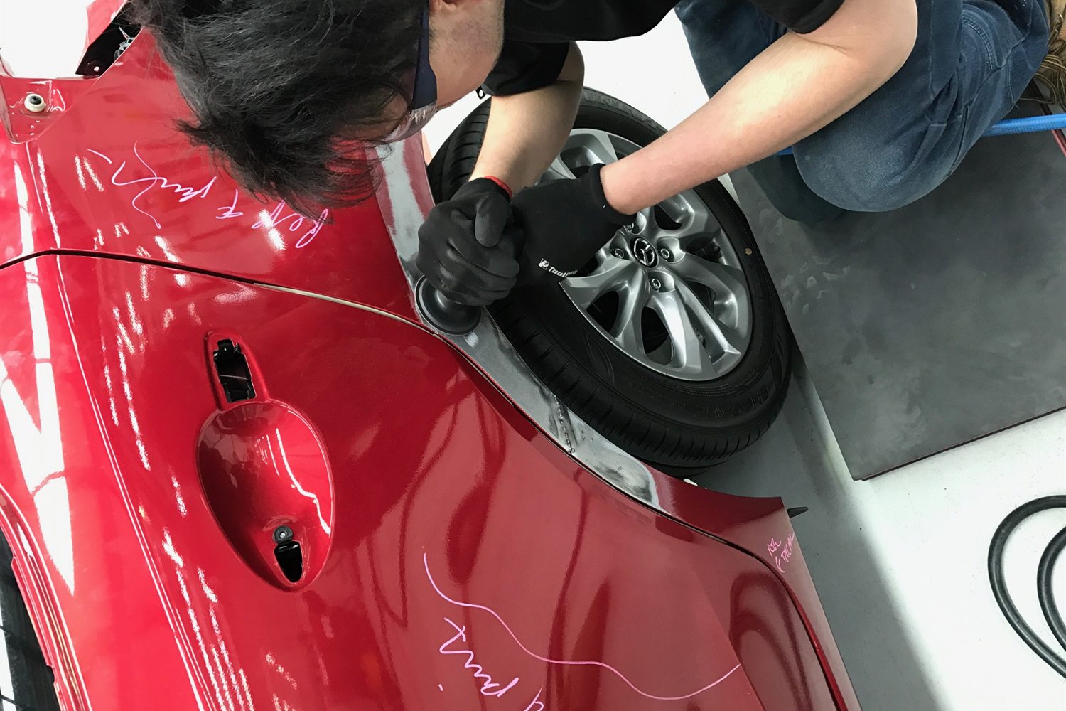 Technician repairing a dent on a red car door at Capital SMART