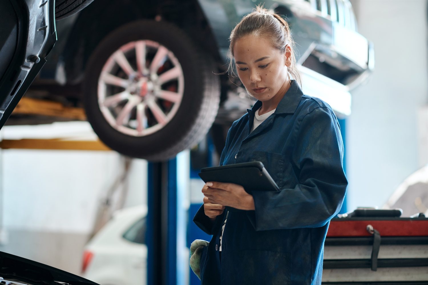 Technician checking a vehicle on a hoist with a tablet