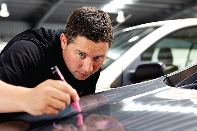 Technician marking hail dents on a bonnet for repair