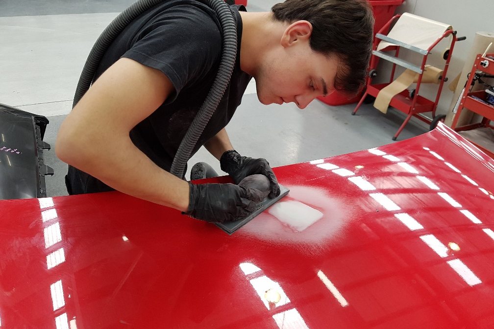 Technician sanding a scratched red bonnet before refinishing